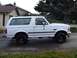 1996 Ford Bronco - White 1996 Ford Bronco parked on a paved surface in front of a house and trees.