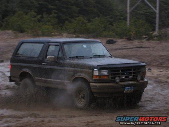 1994 Ford Bronco driving through mud, kicking up spray