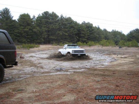 White pickup truck stuck in mud, black SUV in foreground