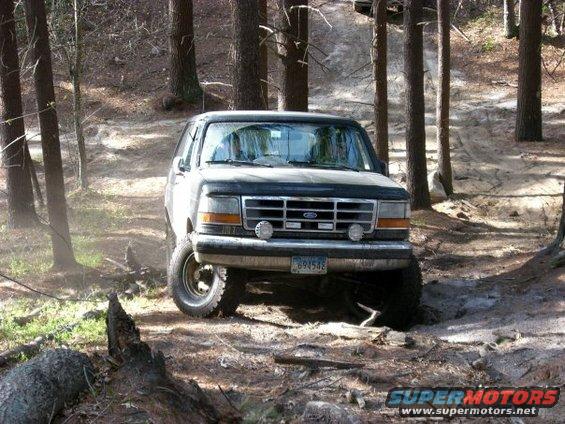 1992 Ford Bronco driving on a wooded dirt trail, front view. License plate reads 694542