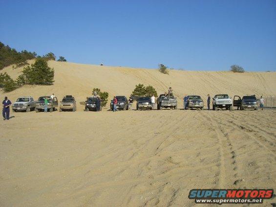 Line of SUVs and trucks on a sand dune under a clear blue sky