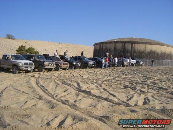 Group of SUVs and trucks on sand dunes with a large concrete structure