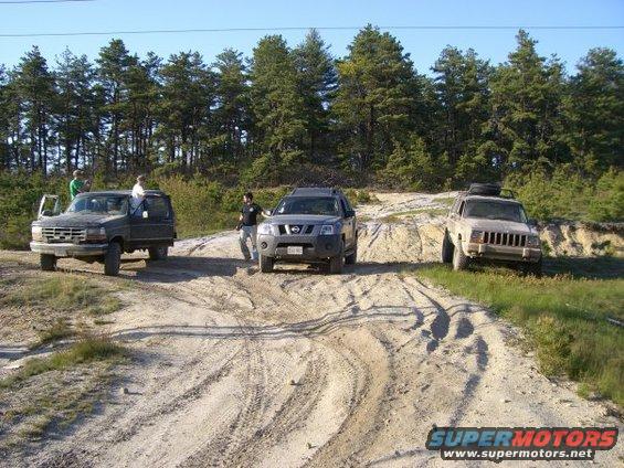 Three SUVs driving on a dirt track with trees in the background