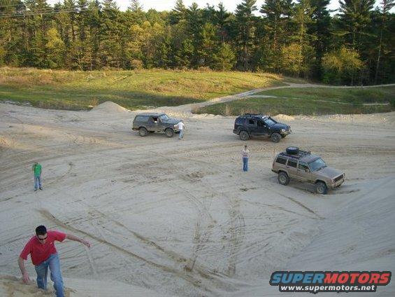 three SUVs parked in a dirt lot with trees in background, people standing around