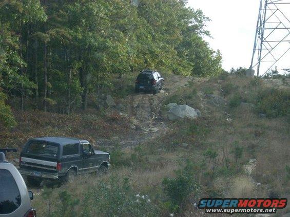 Black Ford Bronco with silver trim driving on a dirt hill, rear quarter view
