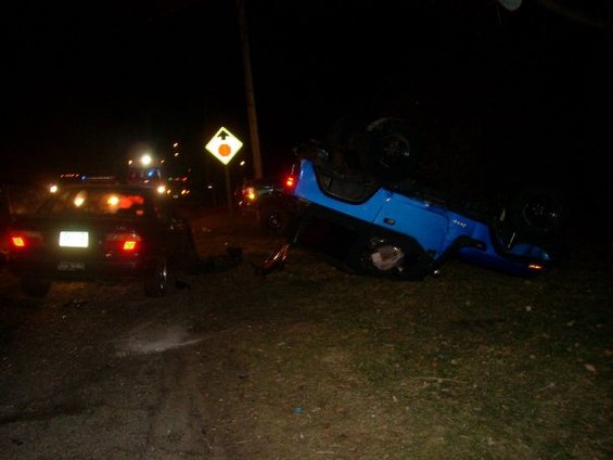 Overturned blue Jeep Wrangler on its side next to a police car at night