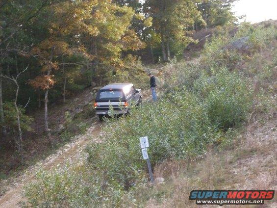 Ford Bronco driving up a dirt path in woods. Person stands nearby