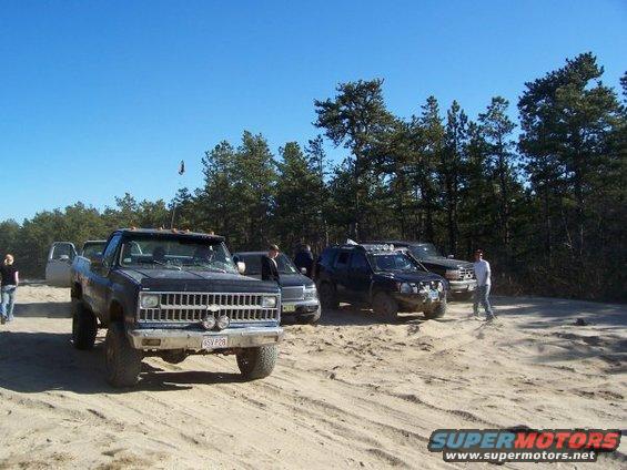 Black pickup truck with lifted suspension and off-road tires, parked on sand