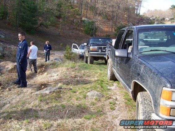 Three trucks parked on a dirt road with people standing nearby