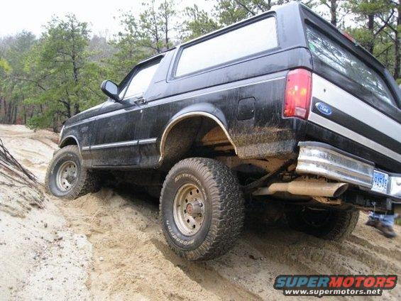 Black 1994 Ford Bronco driving on a sandy trail with trees in the background