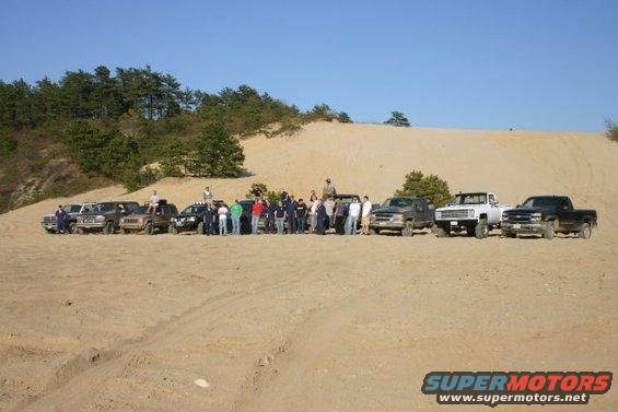 Group of off-road trucks and SUVs parked on a sandy dune with people standing around them