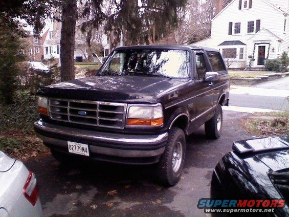 Dark Ford Bronco parked in driveway, house in background. Another car partially visible