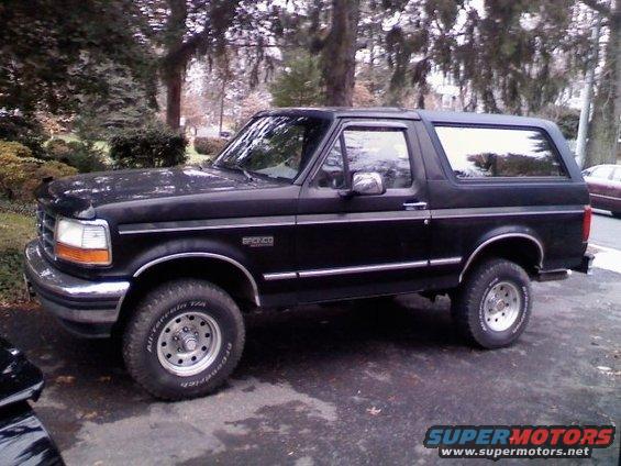Black 1994 Ford Bronco SUV parked on asphalt, side view, with trees and a house in the background