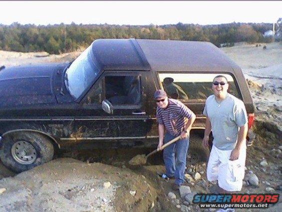 Black Ford Bronco stuck in dirt, side view, with two men nearby