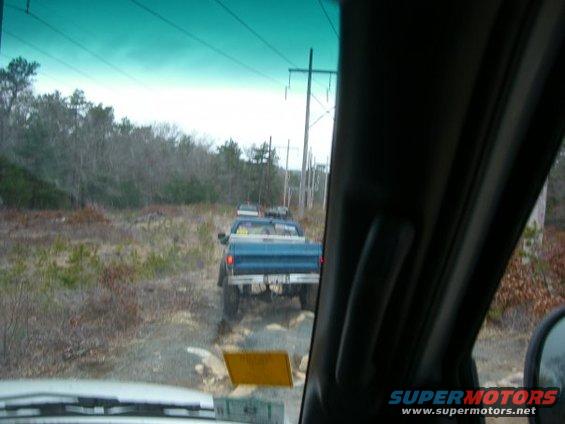 Driving behind a blue pickup truck on a dirt road with trees and power lines