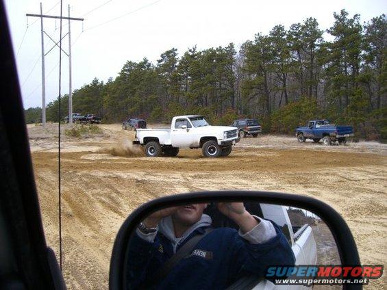 White pickup truck kicking up dust on a dirt road with other trucks and SUVs in the background