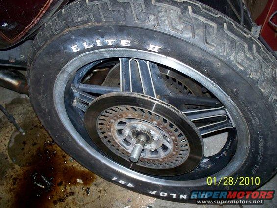 Close-up of a motorcycle wheel with a Dunlop Elite II tire and a brake rotor. Oil is spilled on the ground