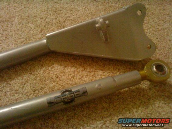 Two silver metal suspension components, one with a 'CAGE' logo, on a carpeted surface