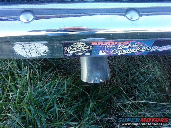 Chrome exhaust pipe protruding from a scratched bumper with a 'Braves 1995 World Series Champions' sticker