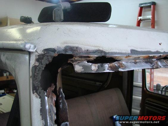 rusted out top of a vehicle's roof, showing interior seats and a ladder in background