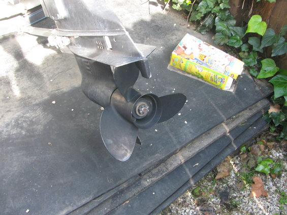 Boat motor lower unit with propeller, resting on a dark surface next to a box of cereal