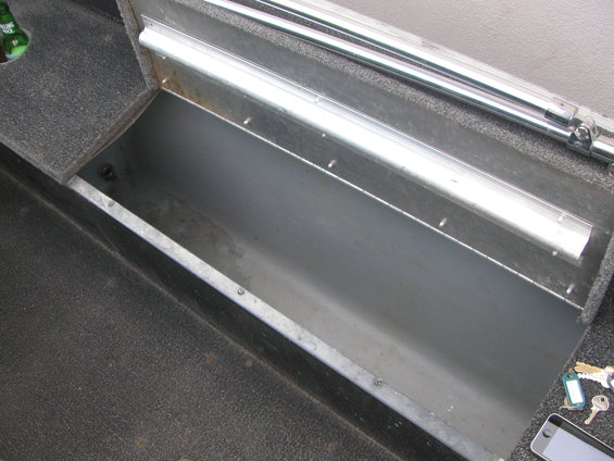 Boat interior storage compartment with metal lining and carpeted edges. Keys and a phone are on the right