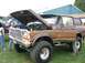 1986 Ford Bronco - A lifted brown Ford Bronco is displayed with its hood open at an outdoor event.