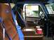 1986 Ford Bronco - The interior of a 1986 Ford Bronco features brown velour seats, blue racing harnesses, and a blue roll cage.