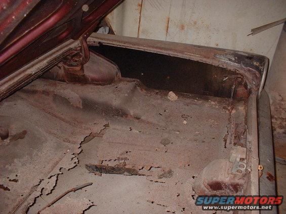 Red car trunk interior with extensive rust damage on the floor and sides