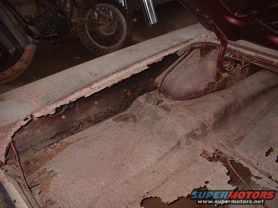 Rusted trunk floor with visible damage and a motorcycle in the background
