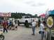 1986 Ford Bronco - A lifted white pickup truck is parked at an outdoor event with people milling around food vendors.