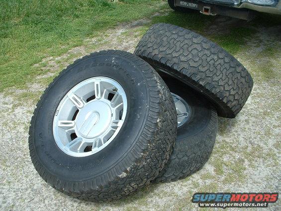Three BFGoodrich tires on alloy rims, one with a silver center cap. Part of a vehicle is visible in the background