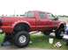 1986 Ford Bronco - A red lifted pickup truck is parked on grass, with a person working underneath it.