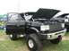 1986 Ford Bronco - A black Ford Bronco is displayed with its hood open at a truck show, with another vehicle visible behind it.
