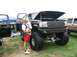 1986 Ford Bronco - A lifted Ford pickup truck with its hood open is displayed at an outdoor event, with a man and child standing nearby.