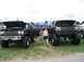 1986 Ford Bronco - Two lifted black Ford trucks are displayed with their hoods open at a truck show, with one identified as a 1986 Ford Bronco.