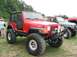 1986 Ford Bronco - A red Jeep Wrangler Rubicon is parked at an outdoor event with other vehicles visible behind it.