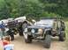 1986 Ford Bronco - Two heavily modified off-road vehicles, a Jeep Cherokee and a Toyota pickup, are displayed at an outdoor event.