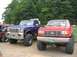 1986 Ford Bronco - Two lifted Ford trucks, a blue one and a red one, are parked side-by-side at an outdoor show.