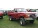 1986 Ford Bronco - A lifted red Ford Bronco is parked on a grassy field with other vehicles and people in attendance.