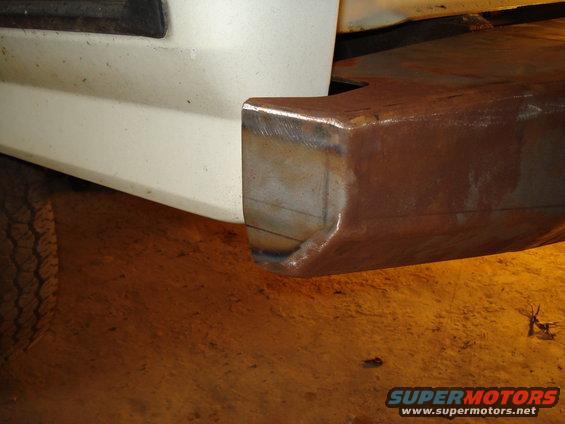 Close-up of a custom metal bumper attached to a white vehicle body, showing welding marks