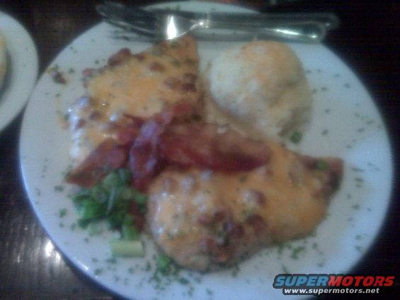 Plate of food with melted cheese and bacon, next to a scoop of mashed potatoes