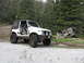 1987 Suzuki Samurai - A white Suzuki Samurai is parked on a dirt road, surrounded by trees, with a dilapidated wooden structure nearby.