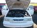 1997 Ford Crown Victoria - The front of a white Ford Crown Victoria is shown with its hood and driver's side door open, revealing the engine compartment.
