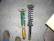 1987 Mazda RX-7 - Comparison of two car shock absorbers, one aftermarket and one stock, on a concrete surface.
