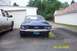 1967 Ford Mustang - A blue 1967 Ford Mustang is parked in front of a garage, with a white pickup truck to its left.