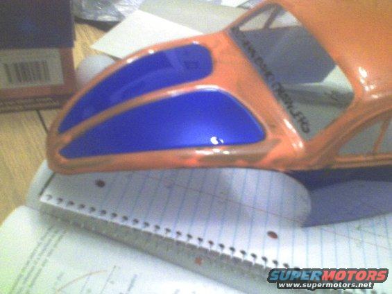 Orange model car body with blue window inserts, resting on a notebook and ruler