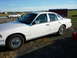 1997 Ford Crown Victoria - A white 1997 Ford Crown Victoria is seen from the side, with another car and a trailer in the background.