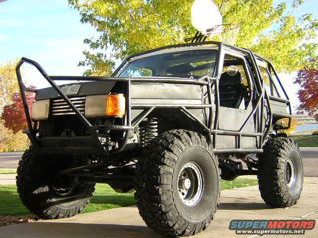 Modified truck with roll cage and large off-road tires. Appears to be a 1993 Ford F-150 base