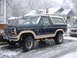 1985 Ford Bronco - A lifted Ford Bronco sits on a snow-covered street in front of houses.